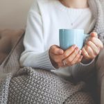 woman bundled in a blanket with a hot drink demonstrating how to stay warm with anemia in winter