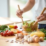 person mixing fresh salad ingredients for cancer prevention